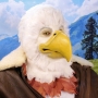 Man wearing latex prosthetic beak and makeup with feathers to look like an anthropomorphic bald eagle.