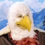 Man wearing latex prosthetic beak and makeup with feathers to look like an anthropomorphic bald eagle.