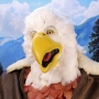 Man wearing latex prosthetic beak and makeup with feathers to look like an anthropomorphic bald eagle.