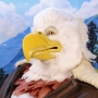 Man wearing latex prosthetic beak and makeup with feathers to look like an anthropomorphic bald eagle.
