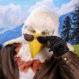 Man wearing latex prosthetic beak and makeup with feathers to look like an anthropomorphic bald eagle with sunglasses.